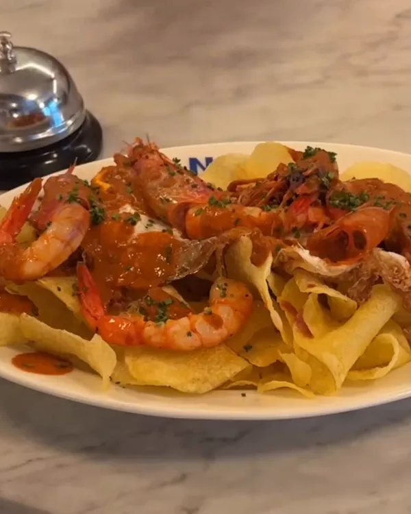 Huevos rotos con gambas rojas y chips de patata, en un plato sobre la barra de mármol