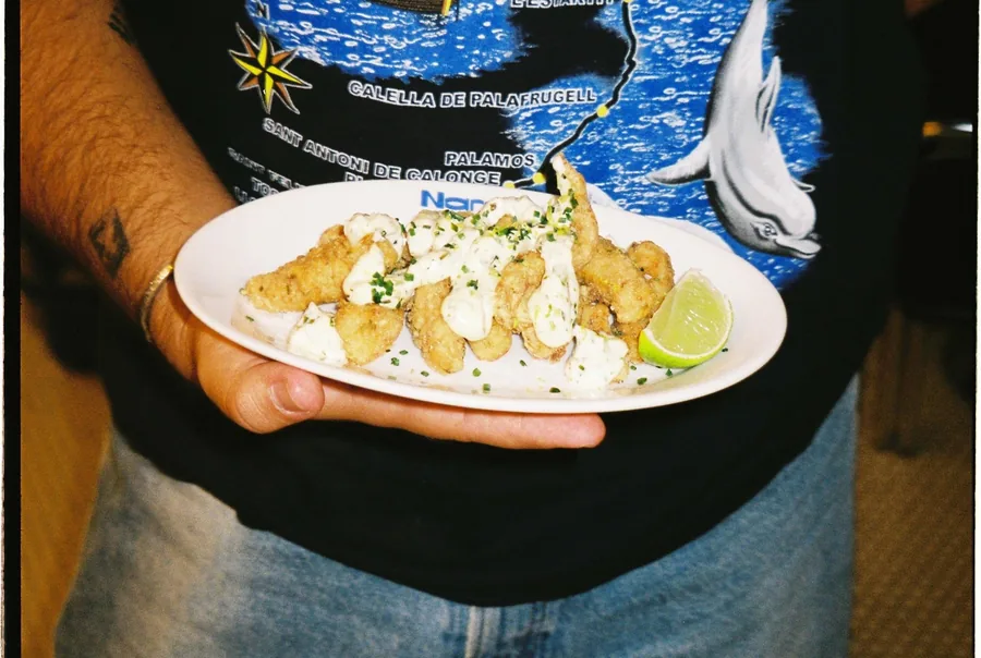 Un camarero lleva a la mesa el plato de fritura con su lima