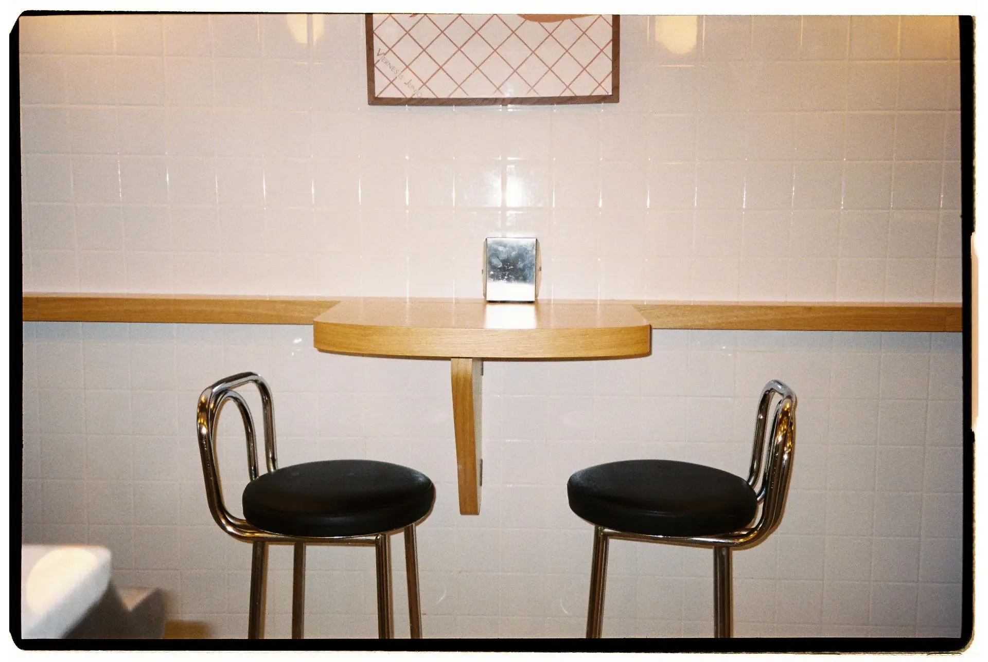 Mesa pequeña con dos sillas negras y un dispensador de servilletas en Taberna Nardi, Barcelona
